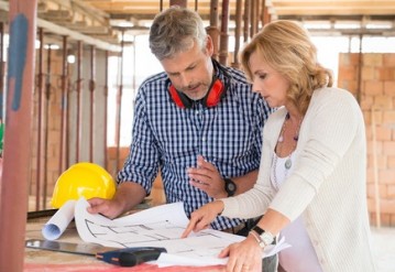 Male architect and woman discussing blueprint plan at construction site