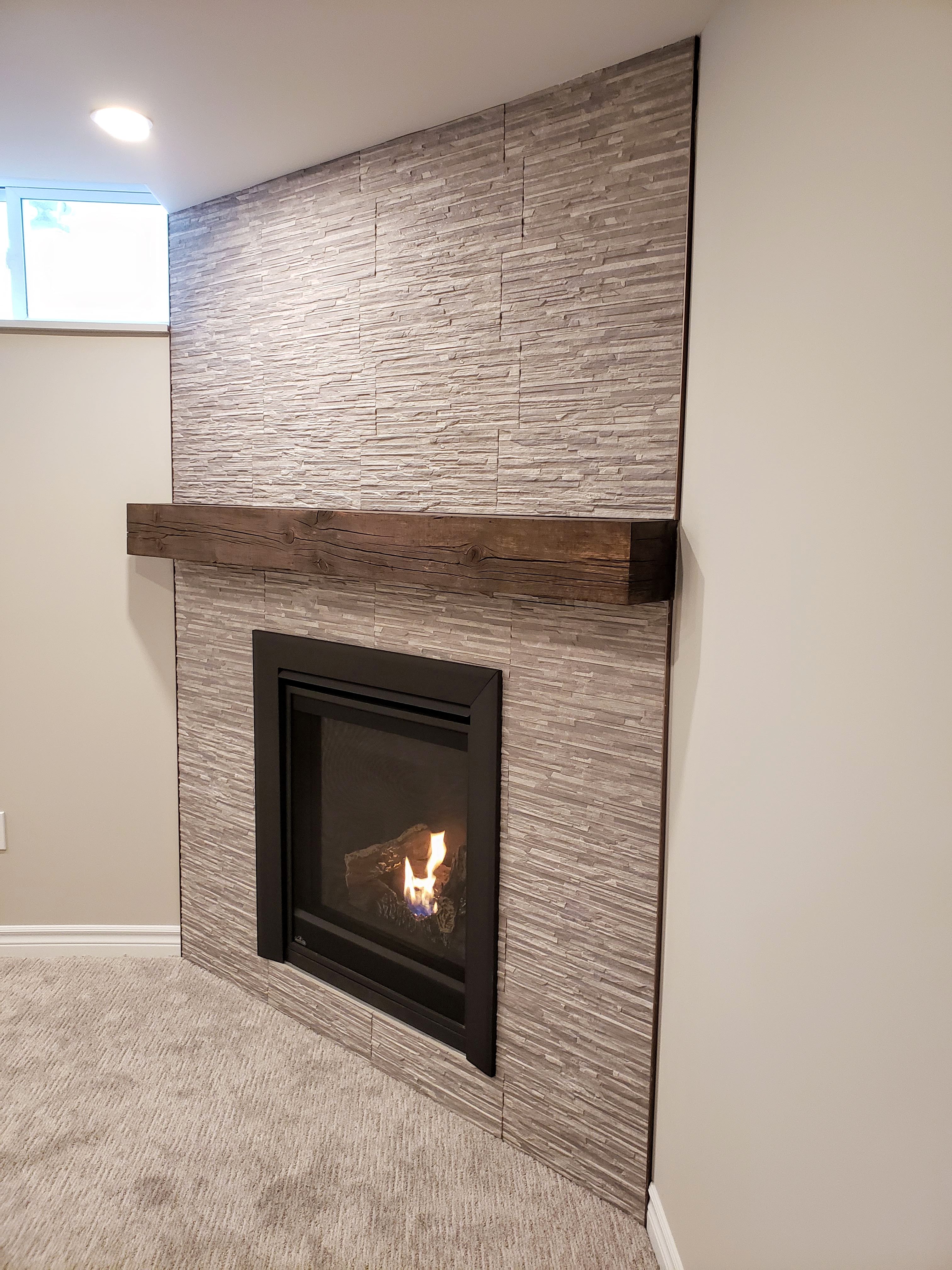 Basement fireplace with tile surround and rustic mantel by Germano Creative Interior Contracting Ltd.