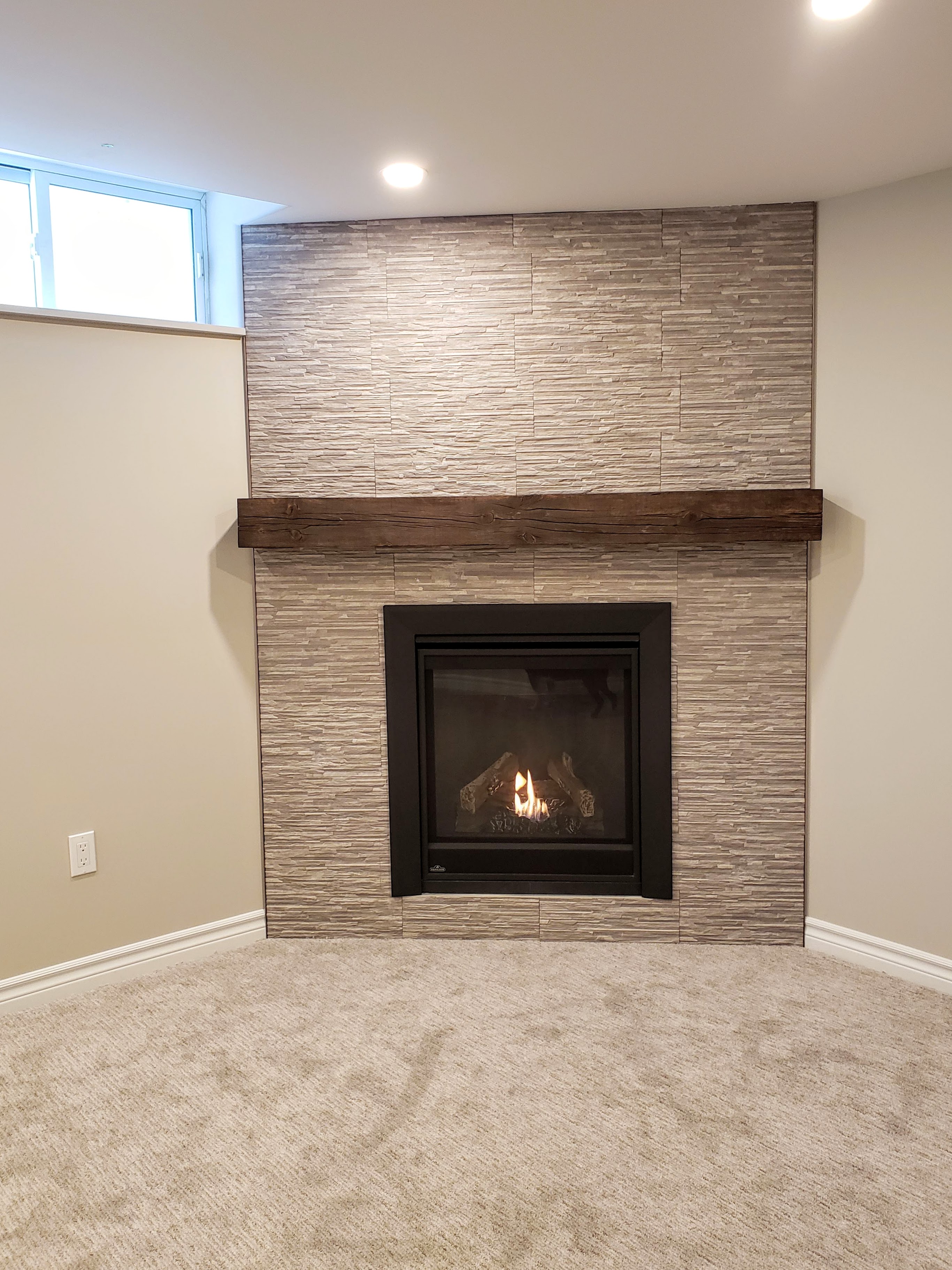 Gas fireplace with tile surround and rustic mantel by Germano Creative Interior Contracting Ltd.