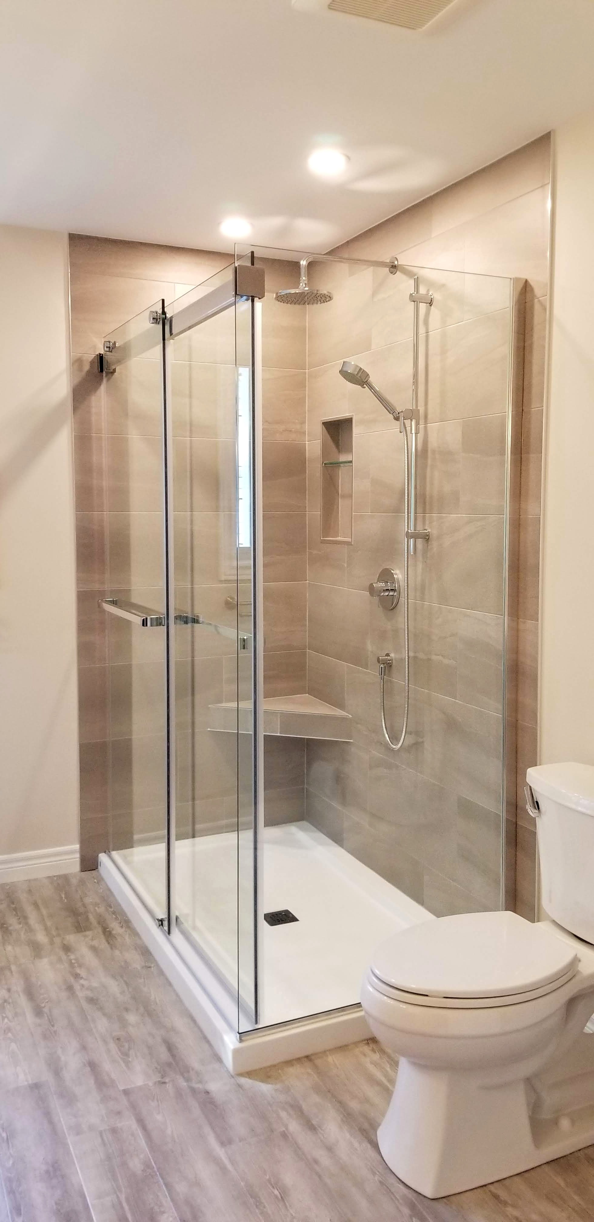Tiled shower enclosed by glass door and panels by Germano Creative Interior Contracting Ltd.